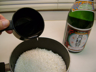 Adding sake/water mixture to rice in a pot