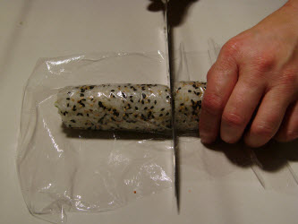 Lay saran wrap over the roll, wet your sushi knife and slice in the center