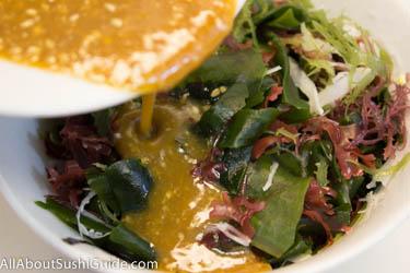 Pouring miso/sesame dressing over seaweed mix