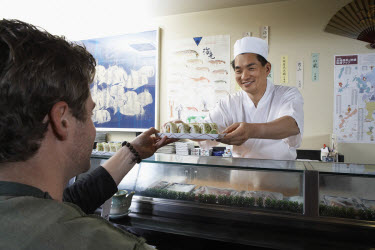 Sushi Chef handing Sushi to Customer over Sushi Bar