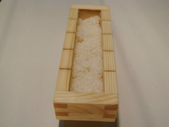 Putting 1/2 cup of rice in oshibako