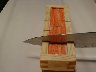 Slicing the oshi sushi using the grooves in the oshibako